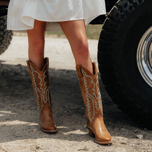 A woman wearing Justin western boots while standing next to a truck.